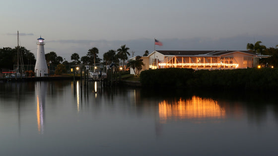 North Fort Myers waterfront at dusk: a small lighthouse, docked boats and a lit waterside restaurant reflected in the water