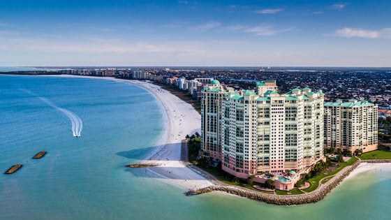 Aerial view of Marco Island in Collier County: a curving white-sand beach, turquoise water and beachfront towers